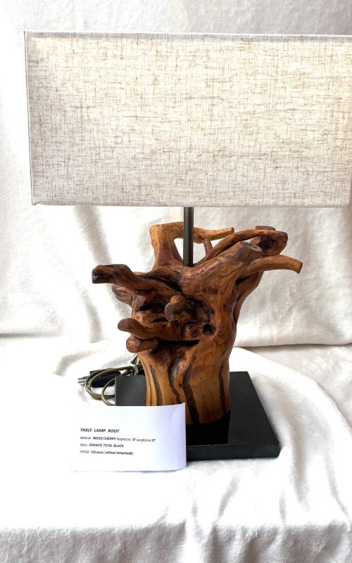 Lampa stołowa z podstawą wykonaną z rzeźbionego kawałka drewna o skomplikowanym, splątanym kształcie. Klosz jest prostokątny, wykonany z jasnej, lnianej tkaniny.