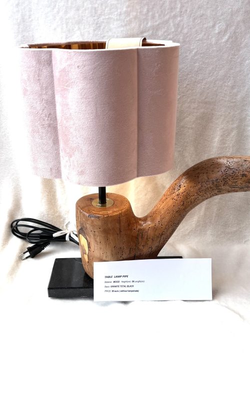 Lampa stołowa z podstawą wykonaną z naturalnego, wygiętego kawałka drewna, przypominającego kształtem dużą fajkę. Klosz jest jasnoróżowy, o pofalowanym, organicznym kształcie.